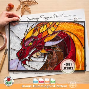 Op de afbeelding: Gebrandschilderd glaspaneel met een drakenkop in rood, oranje en gele tinten. Het kunstwerk is zwart omlijst en bevat de tekst "Fantasy Dragon Panel" en "Hobby Licence". Een bonus kolibriepatroon is ook inbegrepen.