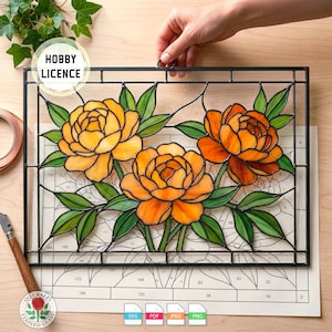 Puede incluir: Panel de vidriera con tres peonías de color naranja y amarillo con hojas verdes, sobre un fondo claro. El panel está enmarcado en negro y sostenido por una mano. Las palabras "HOBBY LICENCE" están en un círculo en la esquina superior izquierda.