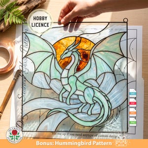 May include: A stained glass dragon pattern with a Hobby Licence. The dragon features green and white wings, set against a yellow and orange sun. Includes a bonus hummingbird pattern. The image also includes the text "Hit me up if you need anytype of custom design".