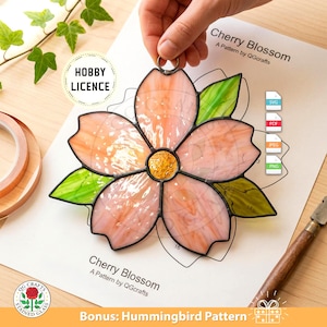 May include: A stained glass cherry blossom with pink petals, a yellow centre, and green leaves. The design is held by a hand. The image includes a pattern sheet with the text "Cherry Blossom" and "Bonus: Hummingbird Pattern."