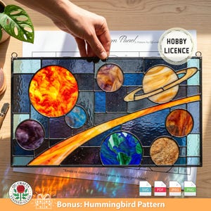 Puede incluir: Panel de vidrieras que representa un sistema solar con planetas y el sol. El panel presenta una variedad de colores, incluyendo naranja, azul, morado y amarillo. El texto "Bonus: Hummingbird Pattern" es visible.