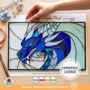 Op de afbeelding: Gebrandschilderd glazen drakenpaneel in blauwtinten, met een zwart frame. Het drakenontwerp heeft ingewikkelde details en wordt door een hand vastgehouden. Het paneel is voorzien van het opschrift "Dragon Panel" en bevat een "Commercial Licence".
