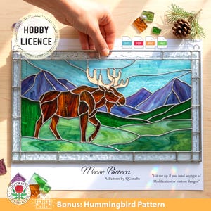 May include: A stained glass panel featuring a moose in a landscape with mountains and green fields. The panel has a light blue sky and is framed in silver. Text on the image includes "Moose Pattern" and "Bonus: Hummingbird Pattern".