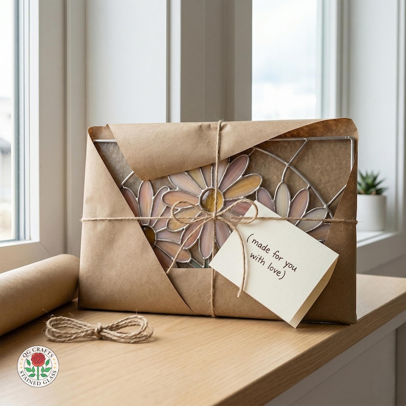 May include: A stained glass daisy design, wrapped in brown paper and tied with twine. A small tag reads "(made for you with love)." The package sits on a wooden surface near a window.