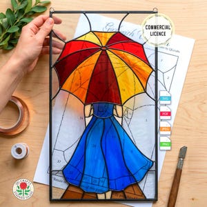 May include: Stained glass panel featuring a woman in a blue dress holding a colorful umbrella. The umbrella has red, orange, and yellow segments. The panel is framed in black and includes the text "Commercial Licence".