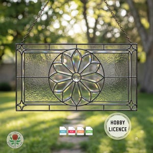 Può includere: Una finestra rettangolare in vetro colorato con un motivo floreale al centro, incorniciata da un bordo in metallo nero. La finestra è appesa a una catena. Il vetro ha un aspetto strutturato. L'immagine include il testo "OG Crafts Stained Glass" e "Hobby Licence".