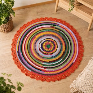 Pode incluir: Um tapete redondo feito à mão com um design vibrante e multicolorido. O tapete apresenta círculos concêntricos de várias cores, incluindo vermelho, verde, amarelo e azul, com uma borda ondulada laranja. O tapete tem aproximadamente 100 cm de diâmetro.