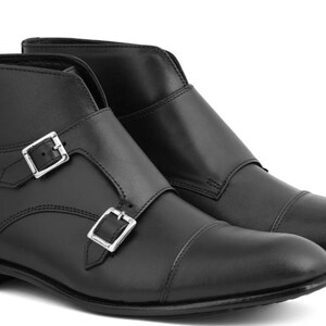 May include: A pair of black leather ankle boots with double monk straps and silver-tone buckles. The boots have a cap toe design and a low heel. The footwear is suitable for various occasions.