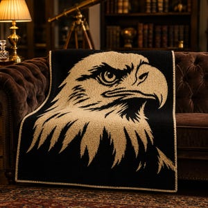 May include: A rectangular crochet blanket featuring a large, detailed profile of a bald eagle head. The design is rendered in contrasting tan and black yarn, with the eagle's features clearly defined against the dark background and a tan border.