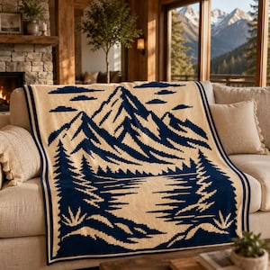 May include: A woven throw blanket featuring a dark blue and cream-colored landscape design. The pattern depicts a mountain range above a forest of pine trees and a body of water. The blanket has a dark blue border and a repeating geometric motif.