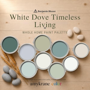 Puede incluir: Una paleta de pintura para todo el hogar Benjamin Moore White Dove Timeless Living con nueve latas de pintura circulares en varios tonos de azul, verde y blanco, dispuestas sobre una superficie de madera clara con espigas de trigo y piedras lisas.