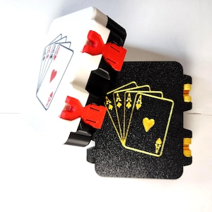 May include: A white and black playing card holder with red accents, displaying a hand of cards. The holder is designed to hold playing cards, with a black base and a white top section. The cards feature red hearts and black spades.