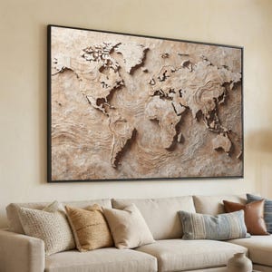 Può includere: Una grande opera d'arte da parete incorniciata con una mappa del mondo dettagliata e strutturata. La mappa, nei toni del beige e del marrone, mostra continenti e oceani in rilievo. L'opera è sopra un divano beige con cuscini decorativi.