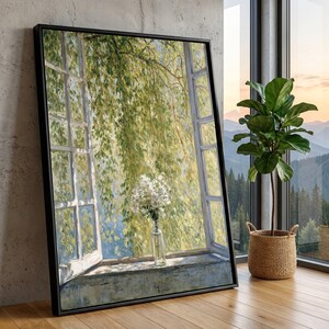 Op de afbeelding: Een ingelijste canvas print van een raamscène. Het kunstwerk toont een open raam met weelderig groen gebladerte en een vaas met witte bloemen. Het zwarte frame leunt tegen een muur.