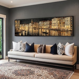 Peut inclure: Une impression panoramique encadrée d'un paysage urbain nocturne, probablement Venise, Italie, est accrochée au-dessus d'un canapé beige avec des coussins décoratifs. L'impression présente des bâtiments illuminés se reflétant dans l'eau. Un tapis à motifs est en dessous.