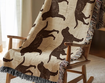 May include: A tan throw blanket with a repeating pattern of brown dog silhouettes. The blanket has a fringed edge and is draped over a wooden rocking chair. The dog silhouettes are in various poses.