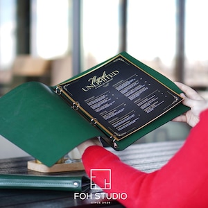 May include: A dark green leather menu binder with a three-ring metal mechanism holding a black menu insert. The menu features gold text that reads "Thanks UNLIMITED A TASTE OF DESSERT" at the top, followed by a list of various dessert items.