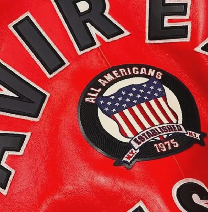 May include: Close-up of a red leather jacket with black and white lettering spelling out "FIRE" and a circular patch. The patch features an American flag design with the words "ALL AMERICANS ESTABLISHED 1975 N.Y."