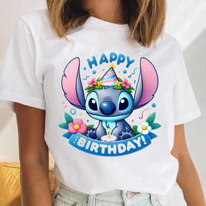 May include: White t-shirt featuring a cartoon character with large ears, wearing a party hat and surrounded by flowers. The design includes the words "HAPPY BIRTHDAY!" on a blue banner.