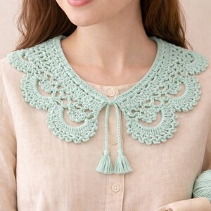 May include: A light green crochet collar with a scalloped edge and a tie closure. The collar has a delicate, openwork design and two small tassels. The collar is a handmade accessory.