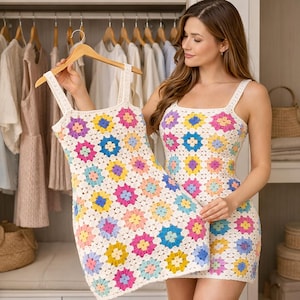 May include: A white crochet dress with a floral pattern in shades of pink, yellow, blue, and purple. The dress has a square neckline and spaghetti straps. The dress is held up by a wooden hanger.