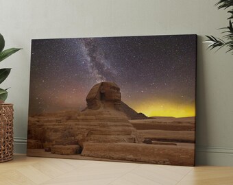 Op de afbeelding: Een canvas print van de Sfinx onder een sterrenhemel. Het kunstwerk toont het oude Egyptische monument in bruin- en beigetinten, met de Melkweg erboven. De print wordt getoond op een lichtgekleurde houten vloer.