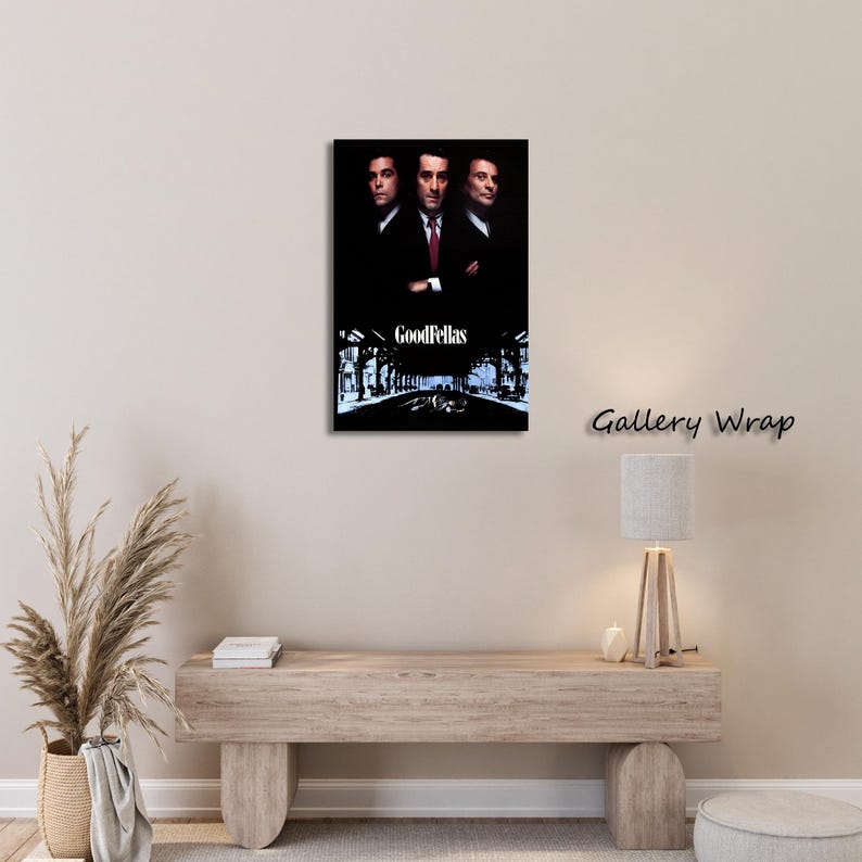 May include: A framed canvas print of the movie "Goodfellas." The artwork features three men in suits against a dark background, with the film's title at the bottom. The print is mounted on a wall above a wooden console.