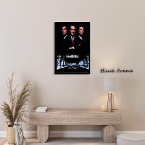 May include: A framed movie poster for the film "Goodfellas" featuring three men in suits. The poster has a black frame and the title is displayed at the bottom. The background is a dark, stylized image of a street.