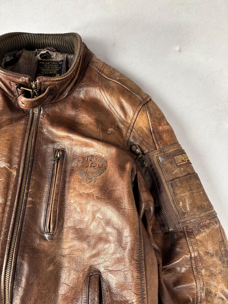 K&ouml;nnte beinhalten: Eine wei&szlig;e Keramik-Tasse mit schwarzem Henkel und dem Text "But First, Coffee" in fetter, schwarzer Schrift. Die Tasse steht vor einem verschwommenen Hintergrund, der eine gem&uuml;tliche Umgebung suggeriert.