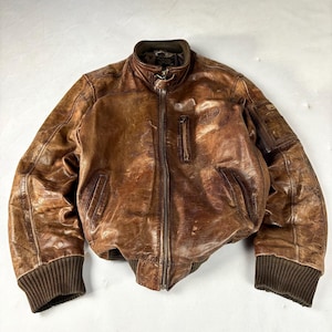 K&ouml;nnte beinhalten: Braune Leder-Bomberjacke mit geripptem Kragen, Manschetten und Saum. Die Jacke hat einen Rei&szlig;verschluss vorne, zwei Vordertaschen und eine kleine Tasche am linken &Auml;rmel. Das Leder hat einen Used-Look.