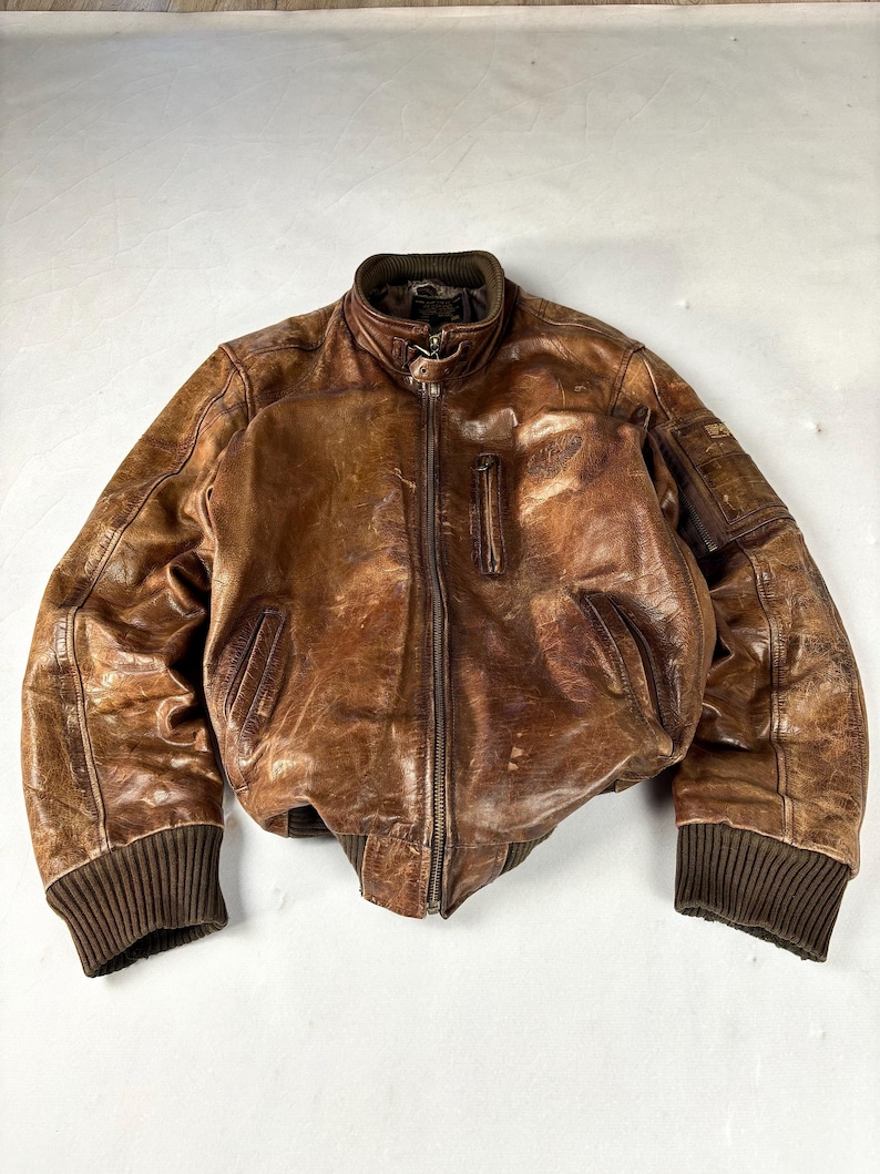 K&ouml;nnte beinhalten: Braune Leder-Bomberjacke mit geripptem Kragen, Manschetten und Saum. Die Jacke hat einen Rei&szlig;verschluss vorne, zwei Vordertaschen und eine kleine Tasche am linken &Auml;rmel. Das Leder hat einen Used-Look.