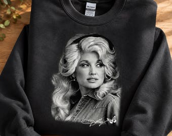 May include: A black crewneck sweatshirt featuring a black and white photographic print of Dolly Parton with voluminous hair and hoop earrings. The graphic includes the signature Dolly in white script text accompanied by a small white butterfly icon.