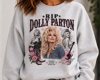 May include: A light gray crewneck sweatshirt featuring a graphic print of Dolly Parton. The design includes the text RIP DOLLY PARTON, LEGEND. QUEEN. FOREVER., and Dolly, along with images of the singer, acoustic guitars, pink roses, and stars.