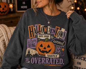 May include: A charcoal gray crewneck sweatshirt featuring a graphic print that reads HALLOWEENTOWN EST. 1998, WHERE BEING NORMAL IS VASTLY OVERRATED. The design includes a central orange jack-o'-lantern, a silhouette of a haunted house, and stars.