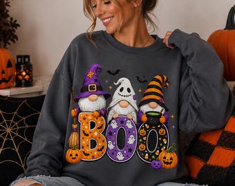 May include: A charcoal gray crewneck sweatshirt featuring a graphic print of three gnomes wearing Halloween hats. The gnomes are positioned behind large letters spelling BOO, decorated with pumpkins, bats, and ghosts in orange and purple.
