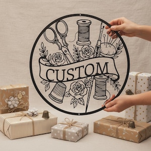 Könnte beinhalten: Schwarzes Metall-Rundschild mit Nähwerkzeugen und dem Wort "CUSTOM" in einem Banner. Das Schild zeigt Schere, Garnrollen, einen Fingerhut und Rosen. Mehrere verpackte Geschenke befinden sich im Vordergrund.