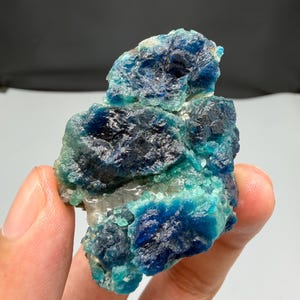 Może przedstawiać: Zbliżenie na żywy, surowy okaz minerału. Kamień charakteryzuje się mieszanką głębokich odcieni niebieskiego, turkusowego i odcieni bieli, tworząc uderzający kontrast. Szorstka tekstura i naturalna formacja minerału są wyraźnie widoczne.
