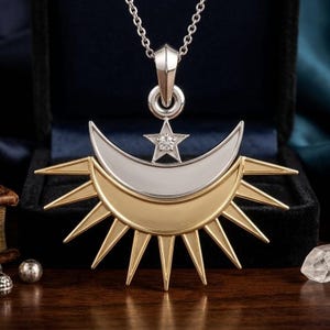 Könnte beinhalten: Halskette mit Anhänger im Himmelsthema. Der Anhänger zeigt einen silbernen Halbmond über einem goldenen Sonnenaufgang. Ein kleiner, funkelnder Stern befindet sich über Sonne und Mond. Die Kette wird in einer schwarzen Schmuckschatulle präsentiert.