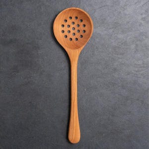 May include: A light brown wooden slotted spoon with a round bowl featuring a grid of circular perforations and a long, smooth, tapered handle. The kitchen utensil displays a natural wood grain pattern throughout its entire surface area.