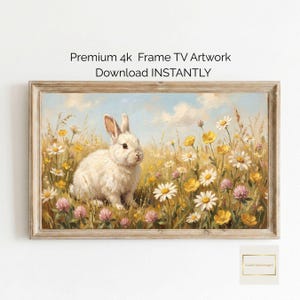 Puede incluir: Una obra de arte enmarcada que presenta un conejo blanco en un campo de flores silvestres. La pintura incluye margaritas, ranúnculos amarillos y trébol rosa bajo un cielo azul. El texto en la parte superior dice "Premium 4k Frame TV Artwork Download INSTANTLY."