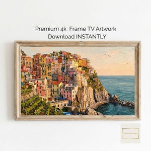 May include: A framed artwork depicting a colorful coastal village on a cliffside, with buildings in shades of pink, yellow, and orange. The sea is a deep blue, and the sky is a soft orange. The text "Premium 4k Frame TV Artwork Download INSTANTLY" is visible.