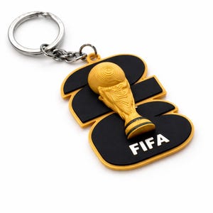 May include: A keychain featuring a gold-colored trophy and the word "FIFA" on a black and yellow background. The keychain has a silver ring and chain.