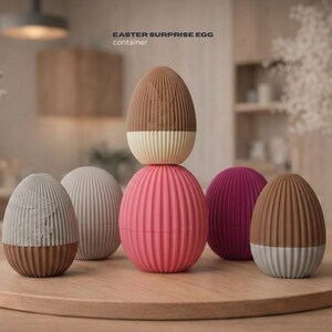 Pode incluir: Uma coleção de recipientes coloridos e canelados em forma de ovo de Páscoa. Os ovos são em tons de rosa, castanho, cinzento e roxo, com um design de duas cores. O texto "EASTER SURPRISE EGG container" é visível. Estão dispostos numa bandeja de madeira.