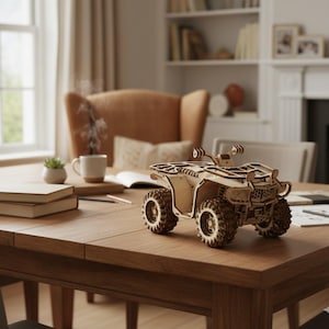 May include: A wooden ATV model with intricate details, including wheels, handlebars, and a seat. The model is made of light-colored wood and sits on a wooden table. The ATV is a miniature replica of an off-road vehicle.