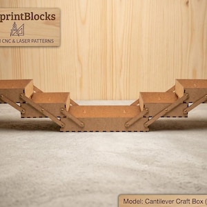 May include: A wooden cantilever craft box with multiple compartments, ideal for storing small items. The box is made of light brown wood and features a hinged design for easy access. The text "BlueprintBlocks" and "PREMIUM CNC & LASER PATTERNS" is visible.