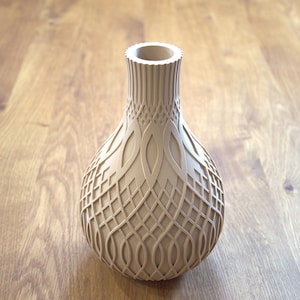 Könnte beinhalten: Eine beige dekorative Vase mit einem komplizierten, geometrischen Muster. Die Vase hat einen bauchigen Körper und einen schmalen, geriffelten Hals. Das Design weist verschlungene Linien und ovale Formen auf, wodurch eine strukturierte Oberfläche entsteht. Die Vase besteht aus hellem Material.