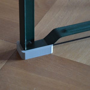 Può includere: Primo piano di un oggetto metallico verde con una base in plastica grigia. L'oggetto sembra far parte di una struttura più grande, forse un mobile o un espositore. La base è rettangolare e poggia su una superficie in legno.