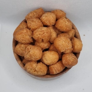 Puede incluir: Un cuenco de madera lleno de bolas de masa fritas redondas y doradas. Los bocadillos tienen una superficie texturizada y están apilados en el cuenco, que se encuentra sobre un fondo blanco. La comida parece recién hecha.