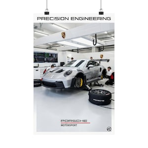 Pode incluir: Um cartaz com um carro desportivo Porsche prateado numa oficina. O carro está num elevador, com mecânicos a trabalhar nele. O cartaz inclui o texto "PRECISION ENGINEERING" e "PORSCHE MOTORSPORT".