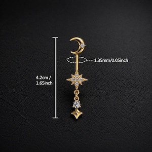 May include: A gold-coloured earring featuring a crescent moon, a starburst, and a dangling star, all adorned with small, clear gemstones. The earring measures 4.2 cm in length and 1.35 mm in width.